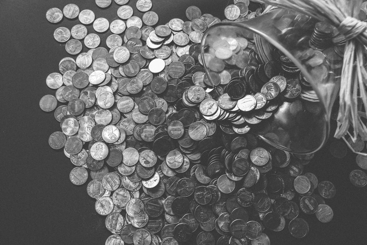 our-story-02 Monochrome image of coins spilling from a glass jar, symbolizing wealth and savings.